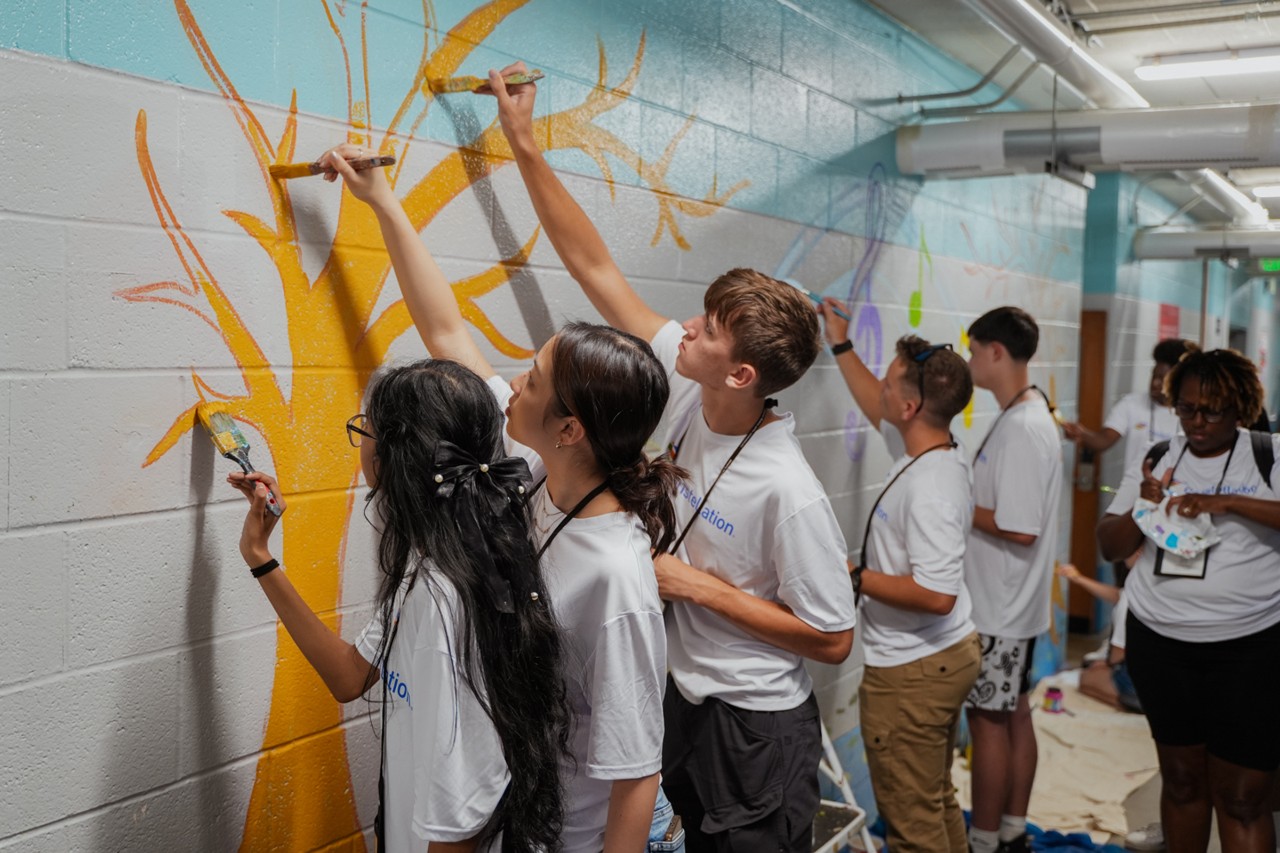 group of y.e.s. students painting a yellow tree mural in a school hallway